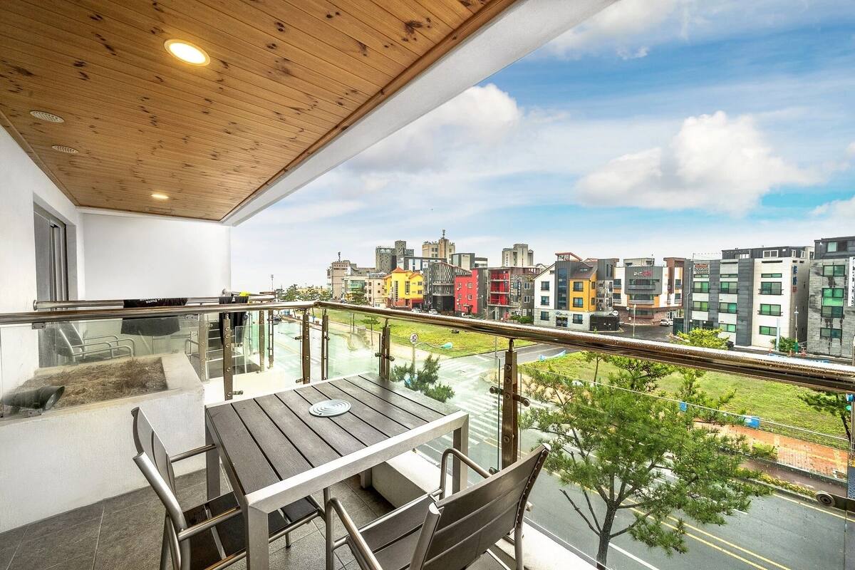 A balcony with a table and chairs, a wooden ceiling, and a view of a cityscape with various buildings.