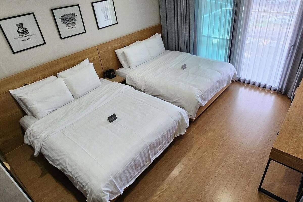 A hotel room with two beds, a wooden headboard, a small table, and a window with curtains.