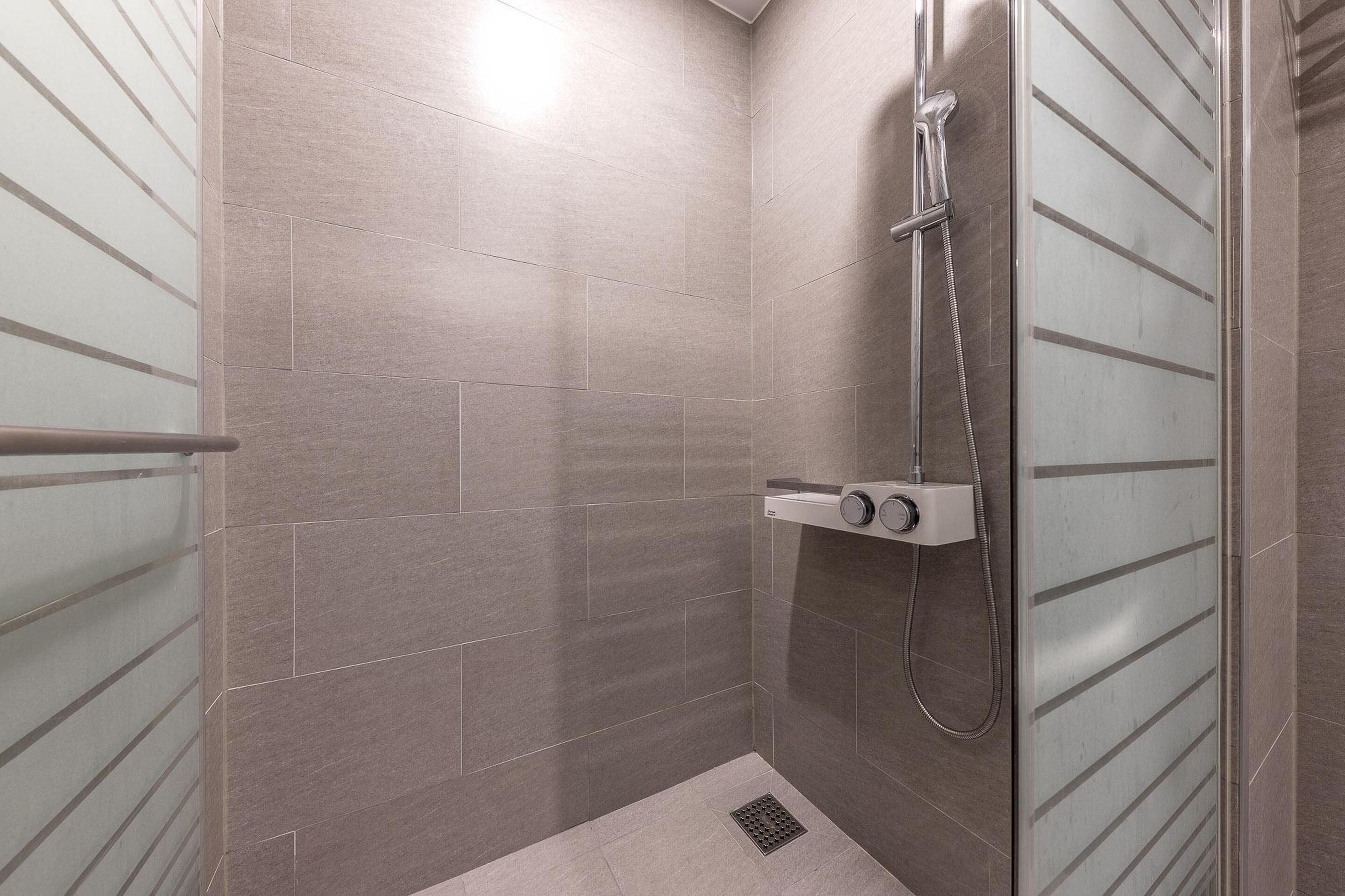 A walk-in shower with a glass door, a handheld showerhead, and a control panel.