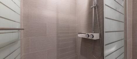A walk-in shower with a glass door, a handheld showerhead, and a control panel.