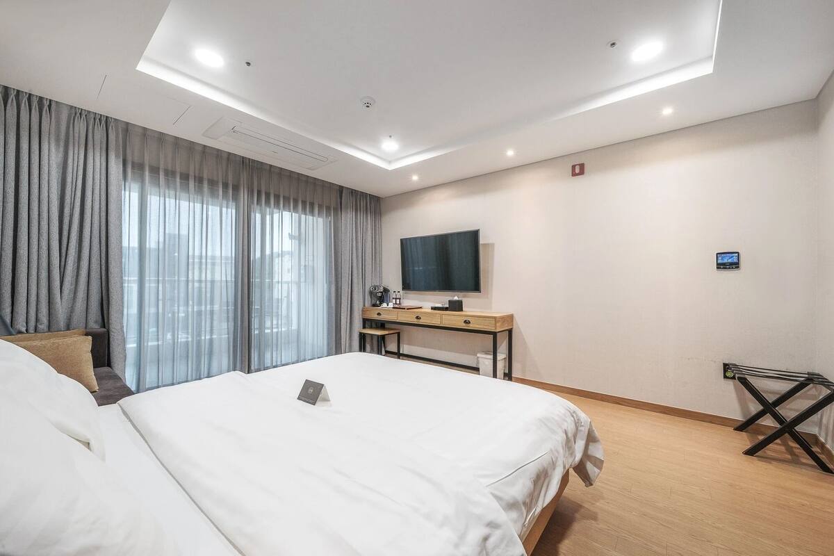 A hotel room with a bed, a desk with a TV, and a window with curtains.