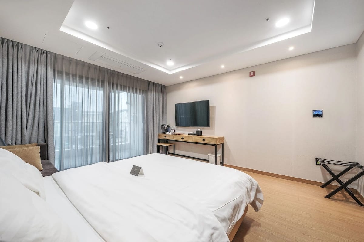 A hotel room with a bed, a desk with a TV, and a window with curtains.