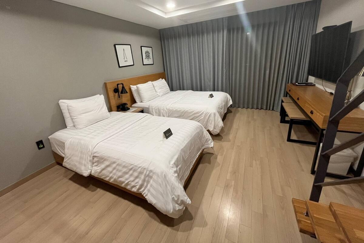 A hotel room with two beds, a desk, a chair, and a TV.
