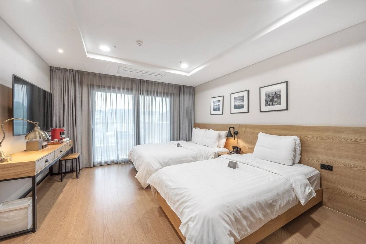 A hotel room with two beds, a desk, a chair, a TV, and a window with curtains.