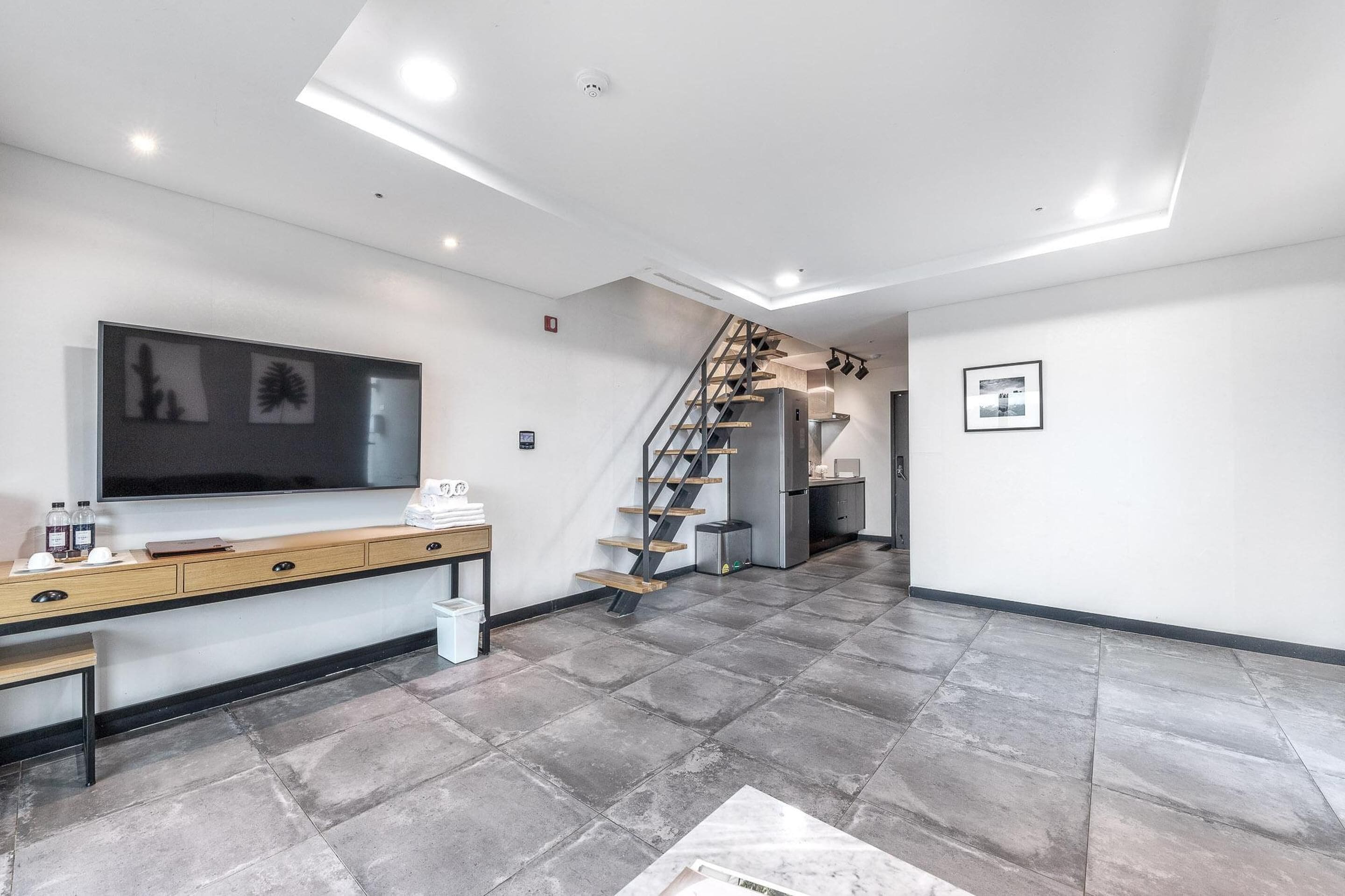 A modern living room with a flat-screen TV, wooden console, and a staircase leading to another level.