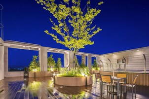 A rooftop terrace with a central tree, seating area, and a bar.