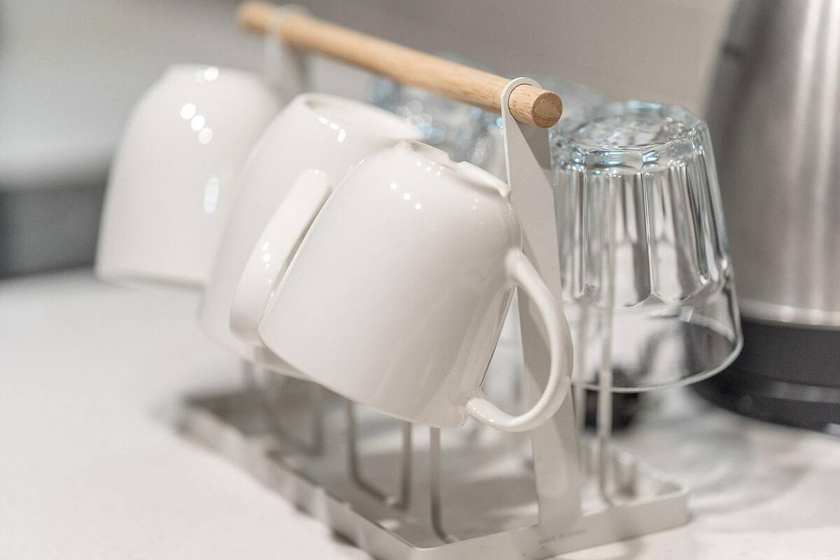 A white mug holder with a wooden handle and a clear glass mug.