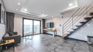 Una habitación de hotel moderna con un ventanal grande, un sofá, un escritorio y una escalera.
