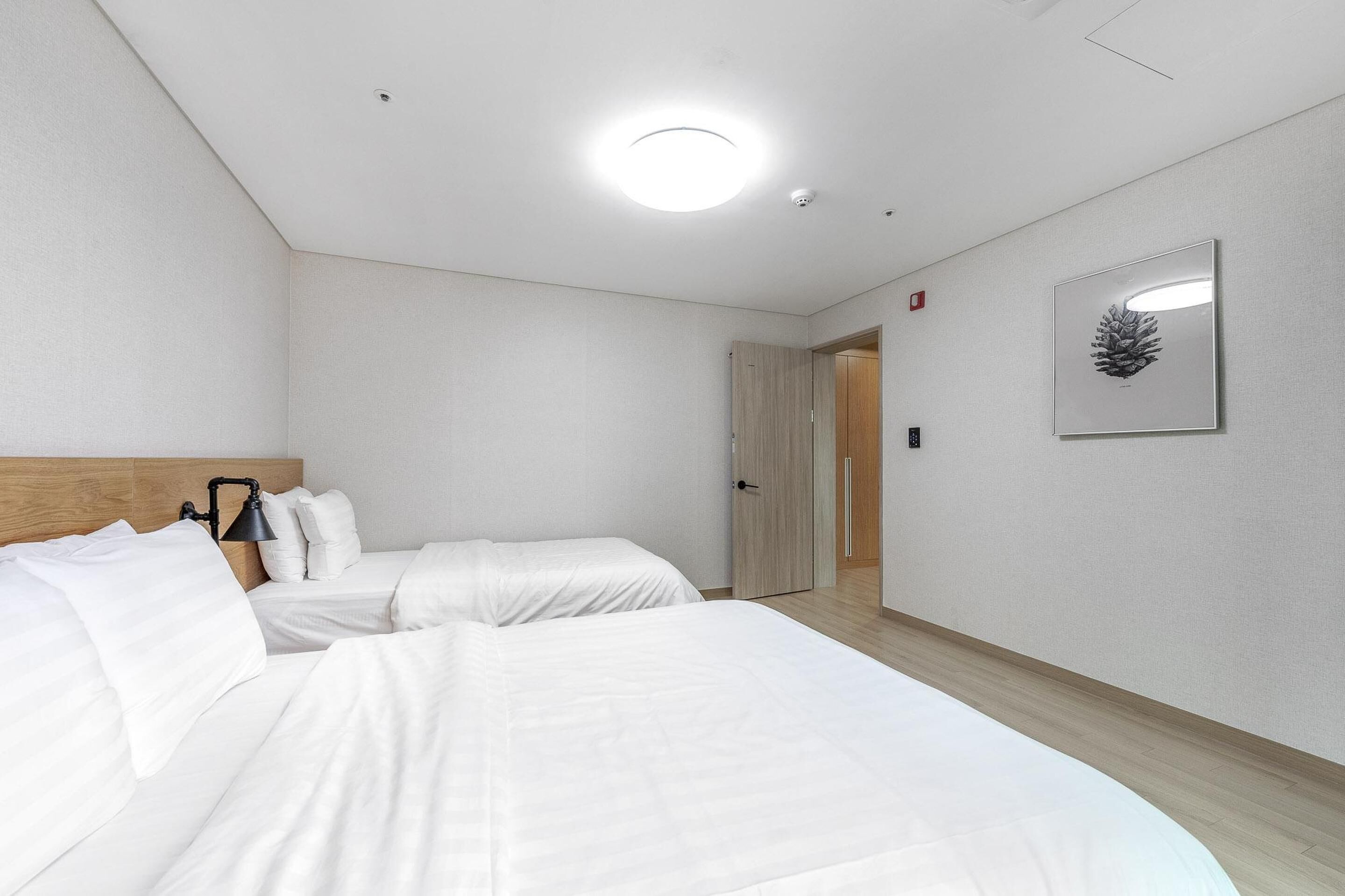 A hotel room with two beds, a wooden headboard, a ceiling light, and a framed pine cone on the wall.