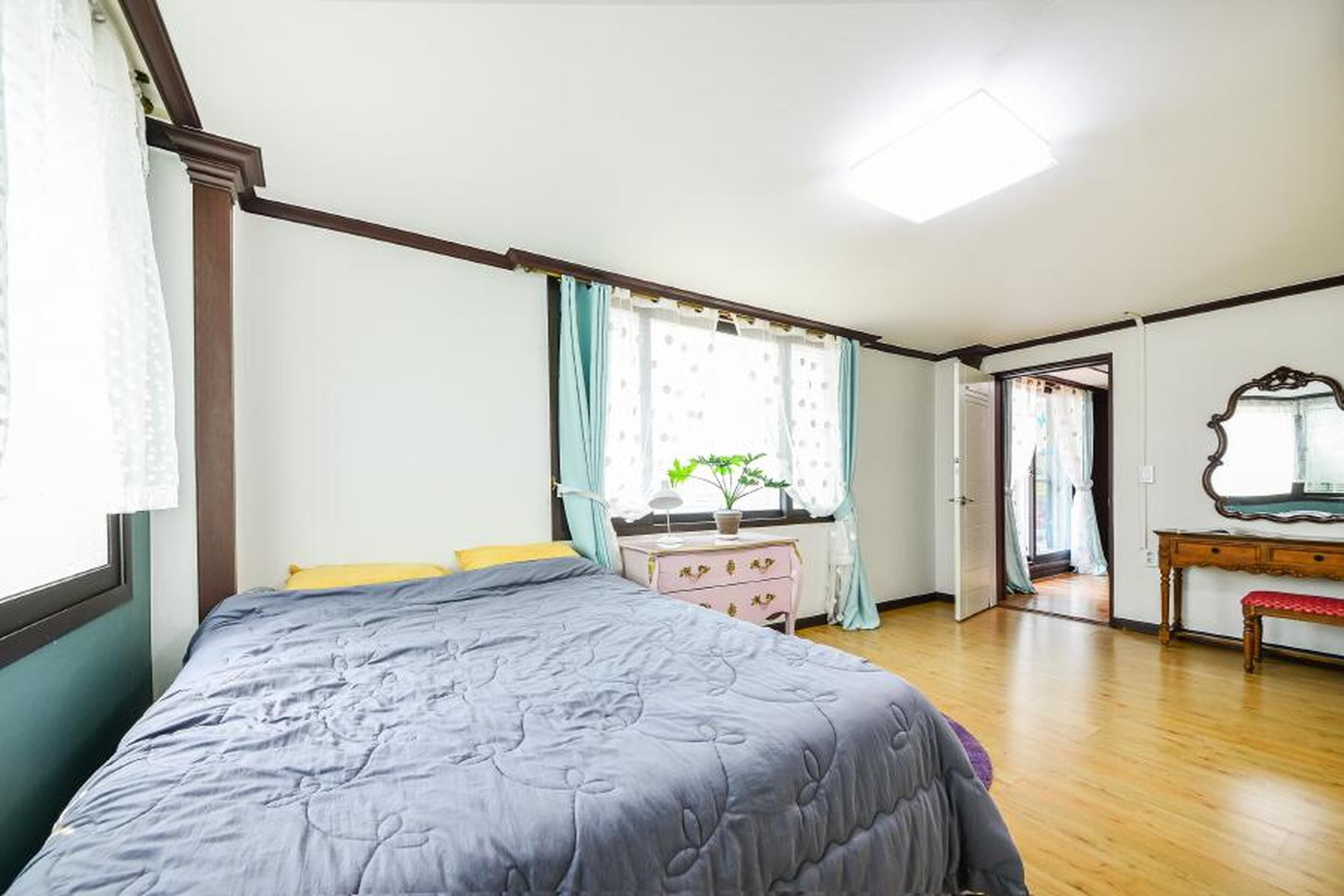 A bedroom with a bed, a dresser, a mirror, and a window with curtains.