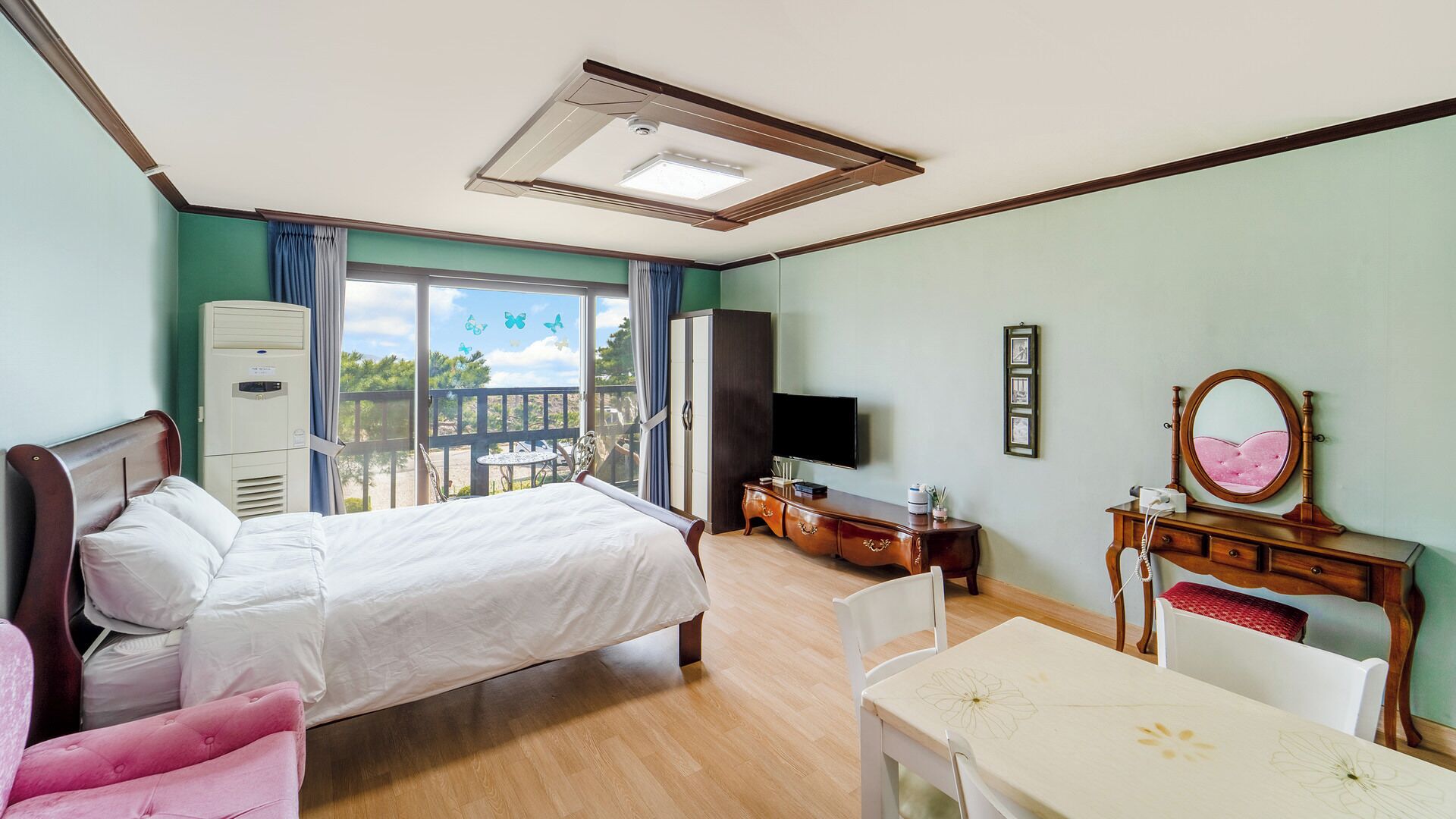 A hotel room with a bed, a desk, a chair, a television, a wardrobe, and a balcony with a view.