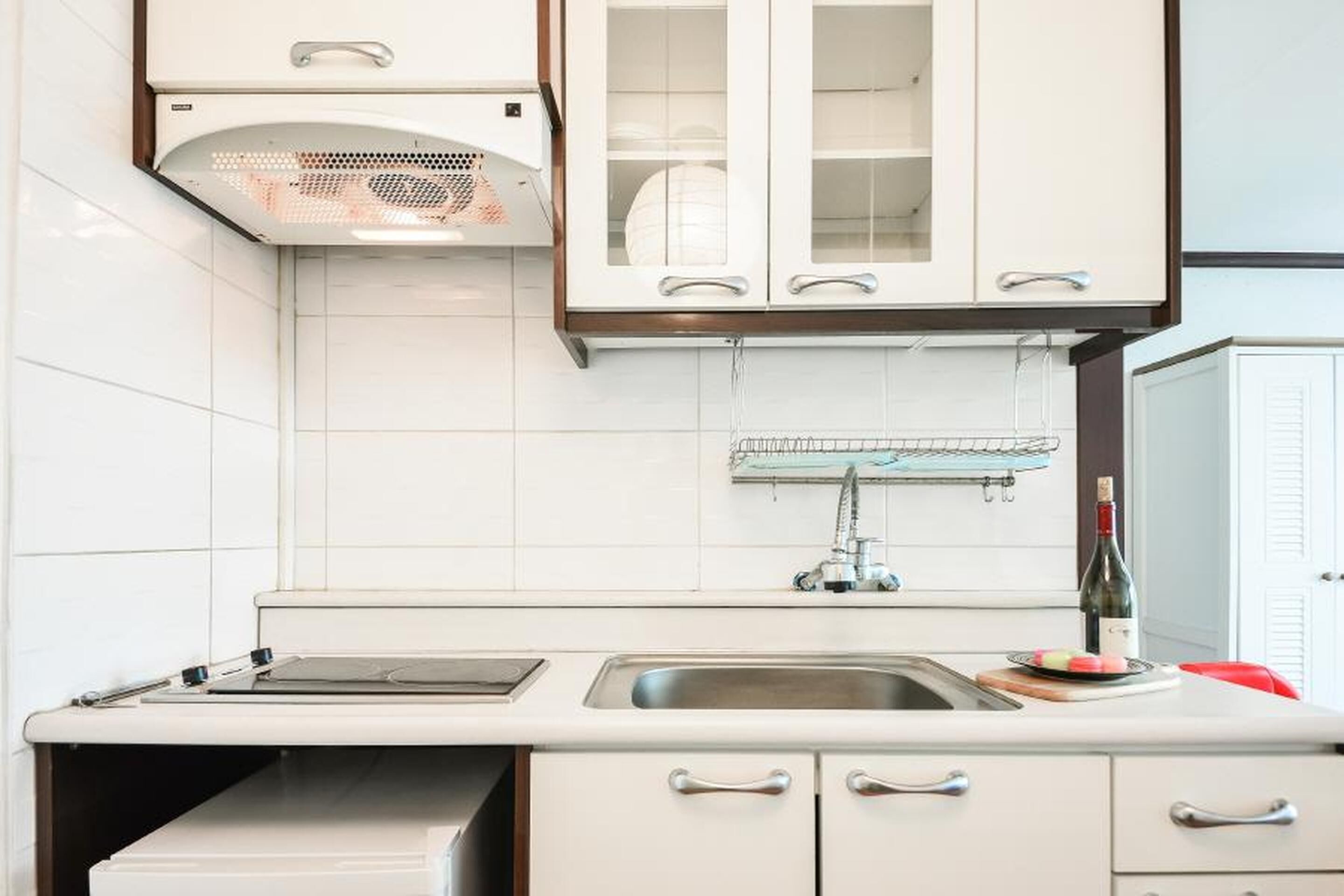 A kitchen with white cabinets, a stainless steel sink, and a wine bottle on the counter.