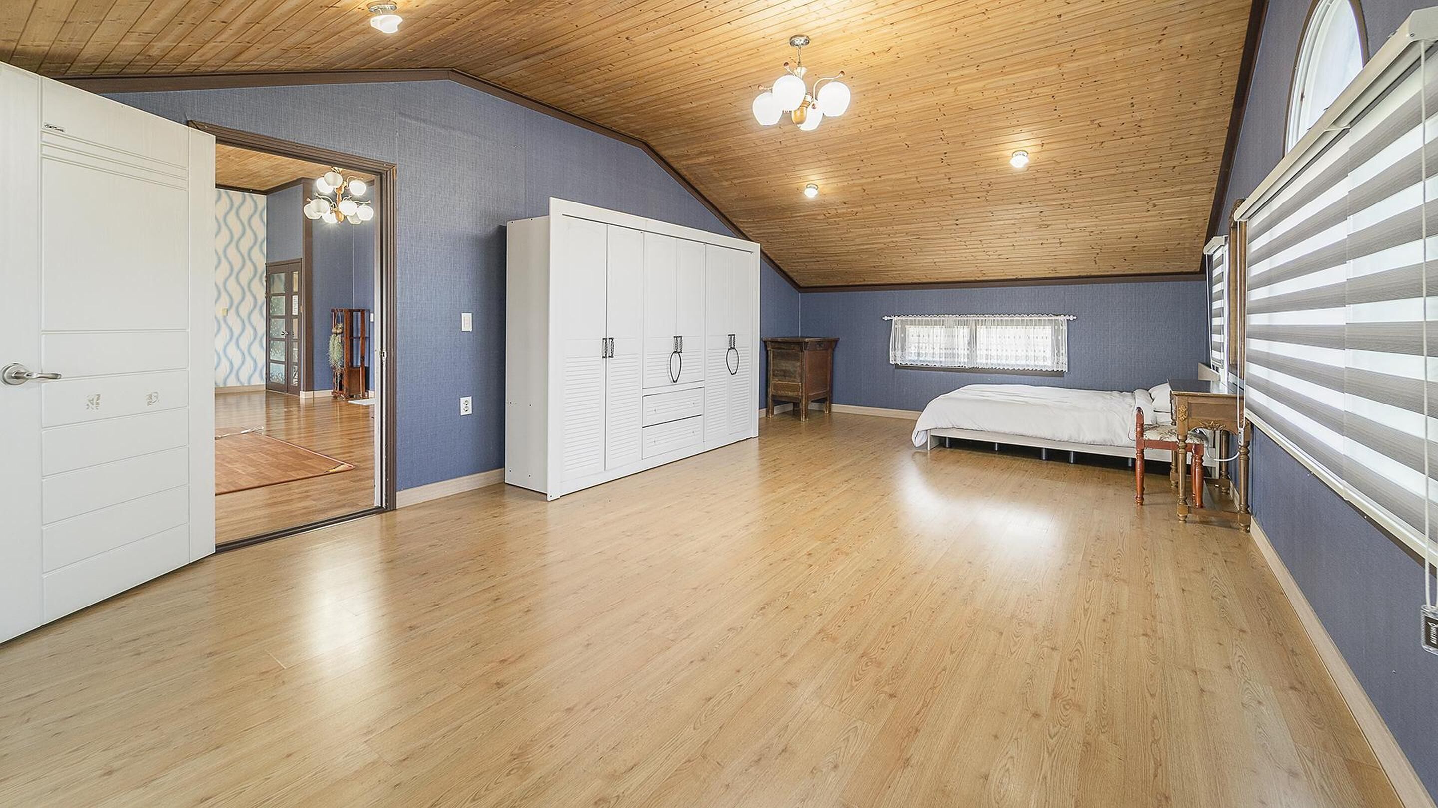 Un dormitorio con techo inclinado, piso de madera, cama, armario y ventana con persianas.