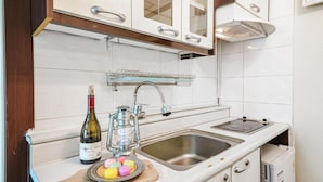 Una cocina con armarios blancos, un lavamanos de acero inoxidable, una botella de vino y un farol.