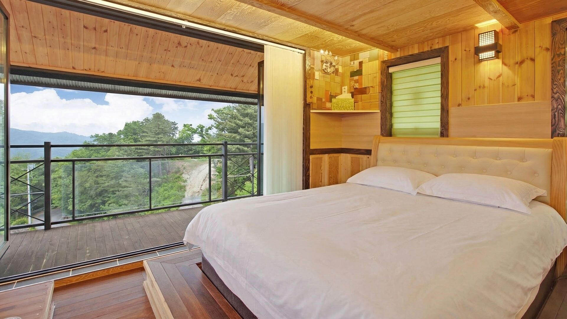 A bedroom with a large window, a bed, and a view of a forested area.