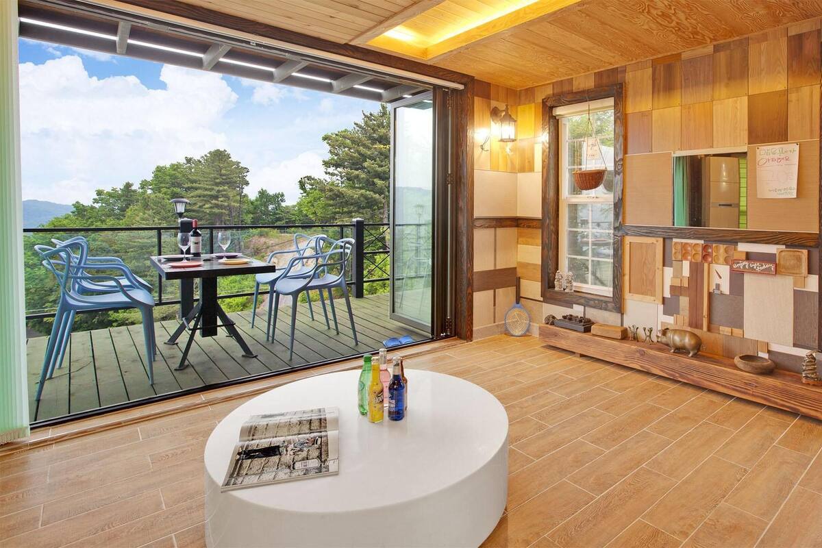 A modern room with a wooden floor, a round white table, and a balcony with chairs.
