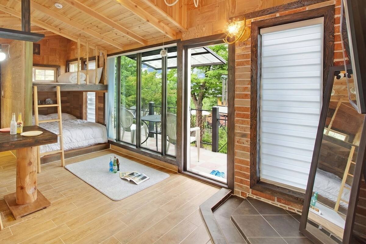 A compact room with a bunk bed, a small desk with a stool, and a large sliding glass door leading to an outdoor patio.