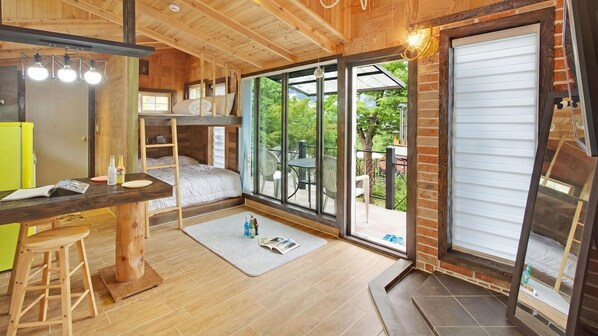 A compact room with a bunk bed, a small desk with a stool, and a large sliding glass door leading to an outdoor patio. - Gapyeong Beethoven House Pension (Gapyeong)