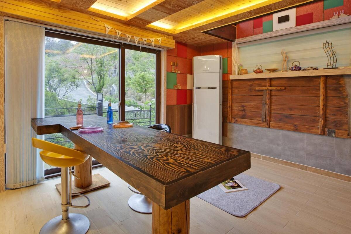 A modern kitchen with a wooden bar, a refrigerator, and a view of the outdoors.