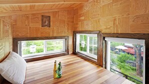 A wooden-paneled room with two windows, a white pillow, and two bottles on the floor.