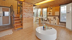 A modern kitchen with a brick accent wall, a wooden staircase, and a round white table with bottles. - Gapyeong Beethoven House Pension (Gapyeong)