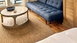 Une pièce avec un canapé bleu, une table ronde recouverte d’une nappe blanche, un luminaire suspendu et une vue sur la mer par une porte vitrée.