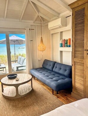 A room with a blue sofa, a round table with a white tablecloth, a hanging light fixture, and a view of the sea through a glass door. - Relax and Unwind at your Private Waterfront Beach Bungalow (Truro)