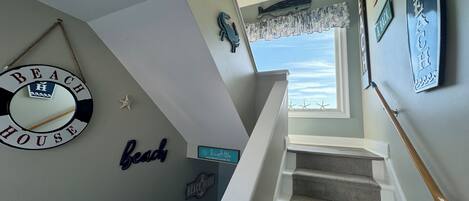 A staircase with a view of the beach through a window, decorated with nautical-themed wall art including a 'Beach House' sign and starfish.