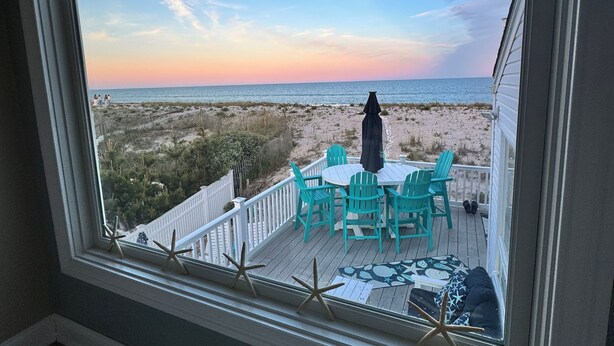 Vista desde una ventana con vista a una playa, con una terraza, sillas y decoración de estrellas de mar.