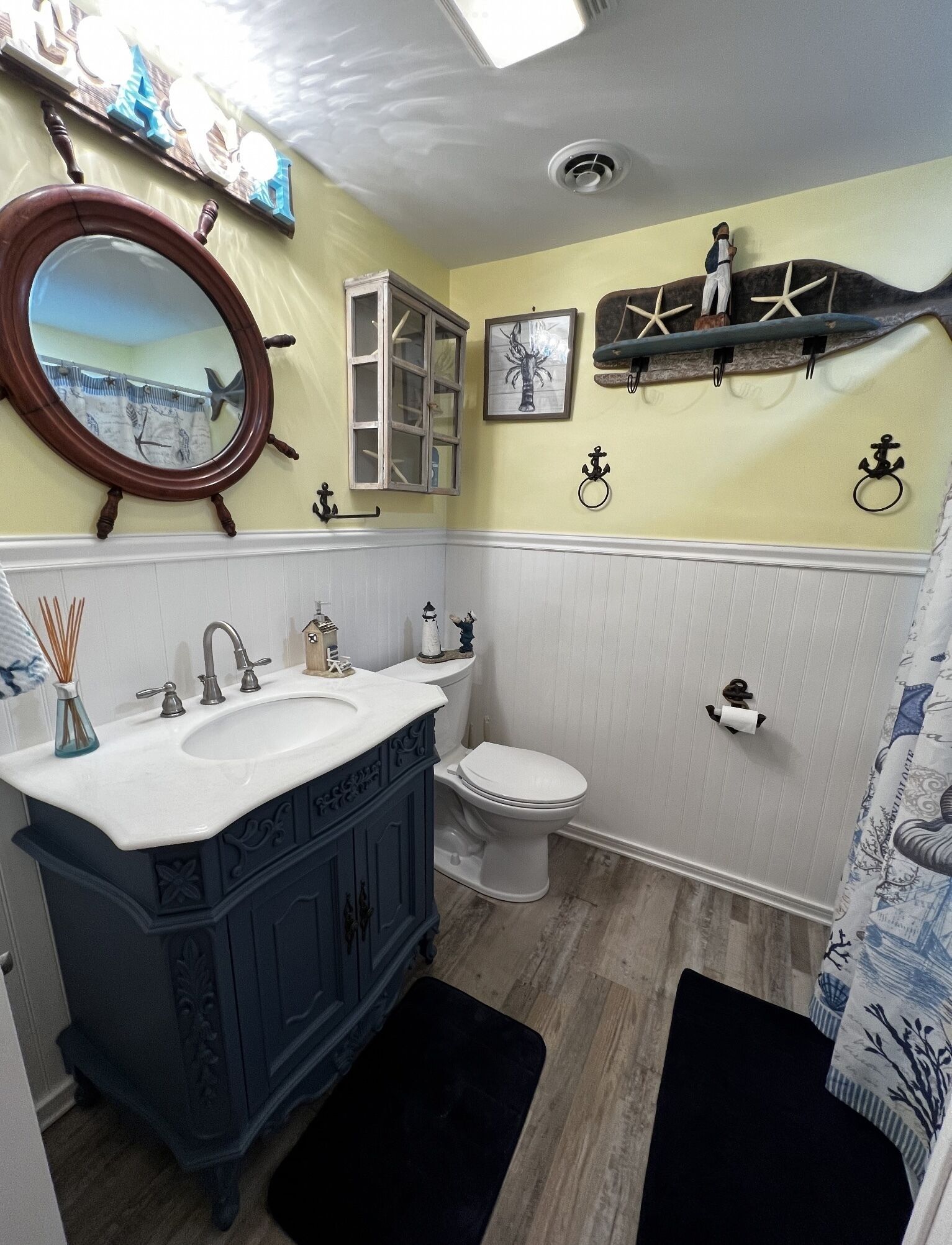 A bathroom with a white toilet, a blue vanity with a mirror, and nautical-themed decorations.