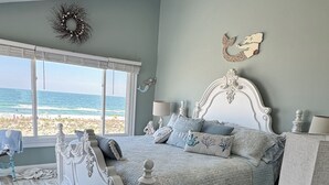 Un dormitorio con una cama grande, vista a la playa y un adorno en la pared.