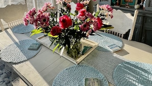 Un comedor con una mesa dispuesta para cuatro, destacando un jarrón de flores rosas, un candelabro y vistas al océano.