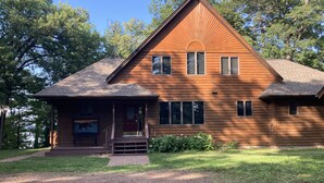 A wooden cabin with a porch, a small staircase, and a view of the surrounding trees.
