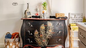 Un ambiente compatto con un mobile nero decorato con motivi a piuma di pavone, una piccola pianta e un cesto a terra.