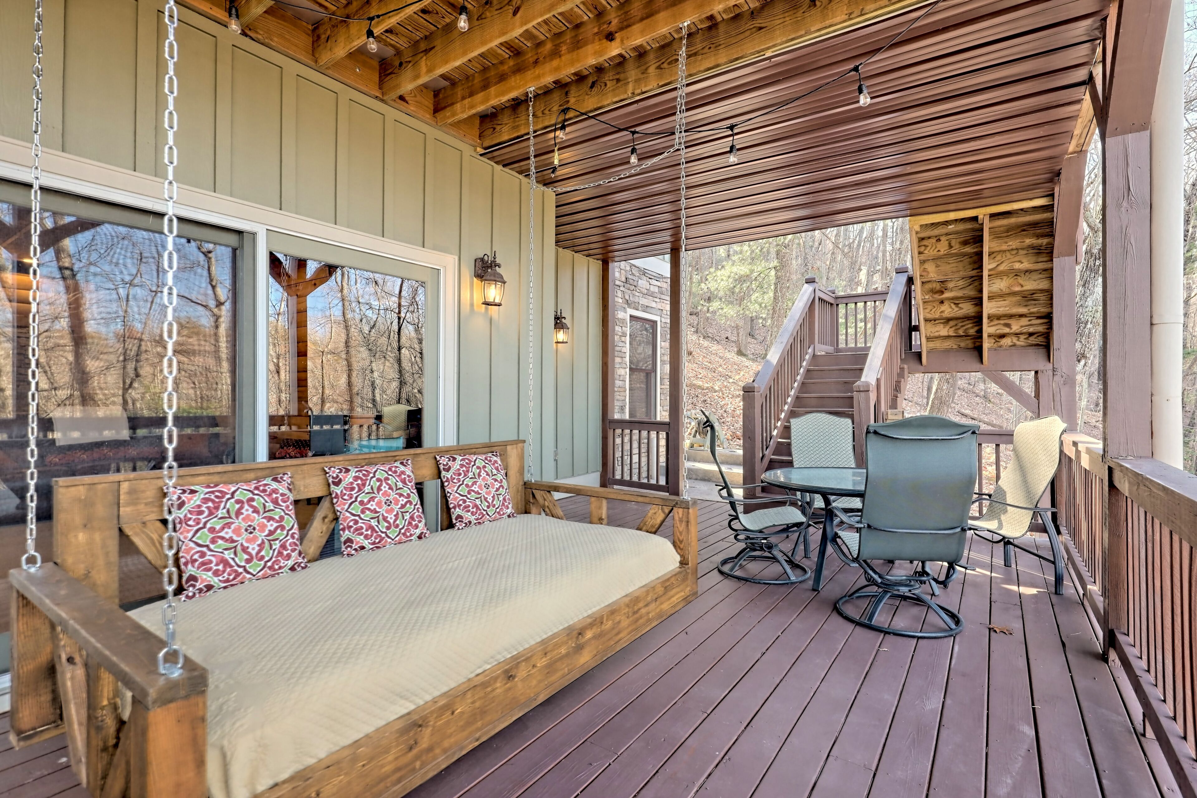 A wooden deck with a swing seat, a table with chairs, and a staircase leading to an upper level.