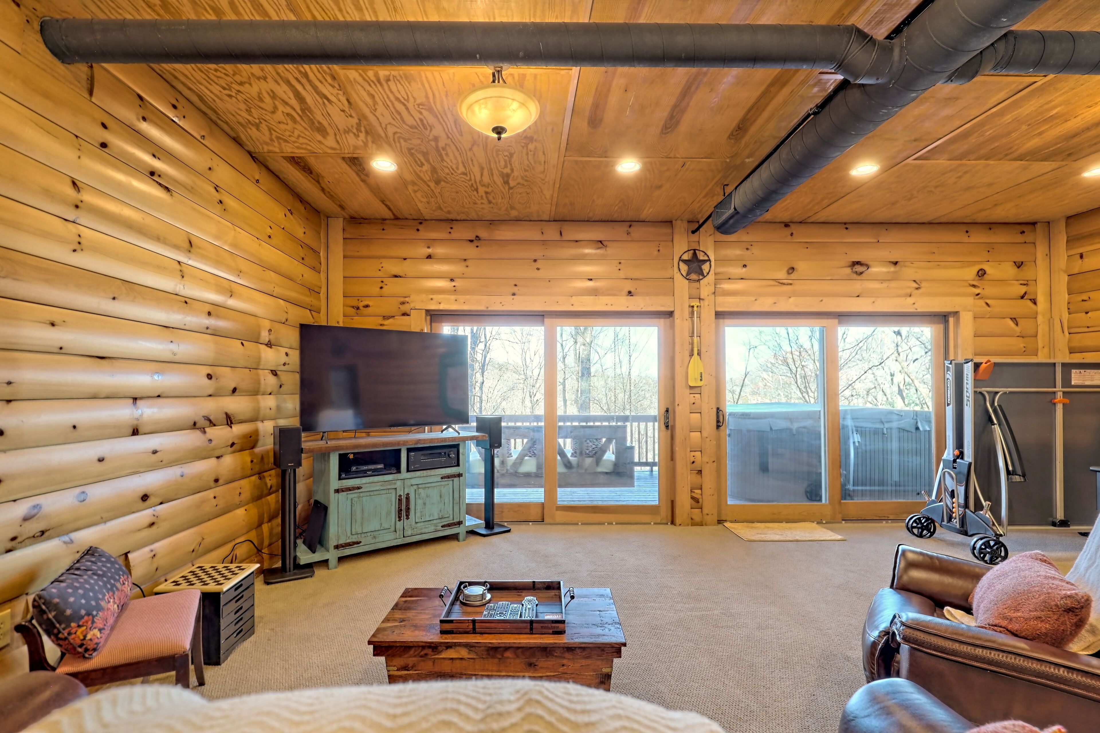 Ein Holzblockhaus-Innenraum mit Holzboden, einem Fernseher, einem Couchtisch, einer Couch und einer Glastür, die auf eine Terrasse führt.