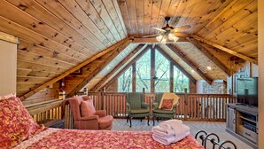 A cozy attic bedroom with a large bed, two chairs, a television, and a fireplace. - Ultra Peaceful Retreat! Large Cabin, 2 Masters on Main, Games & Lake! (Ellijay)