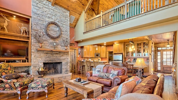 A spacious living room with a stone fireplace, leather sofas, and a wooden dining area. - Ultra Peaceful Retreat! Large Cabin, 2 Masters on Main, Games & Lake! (Ellijay)