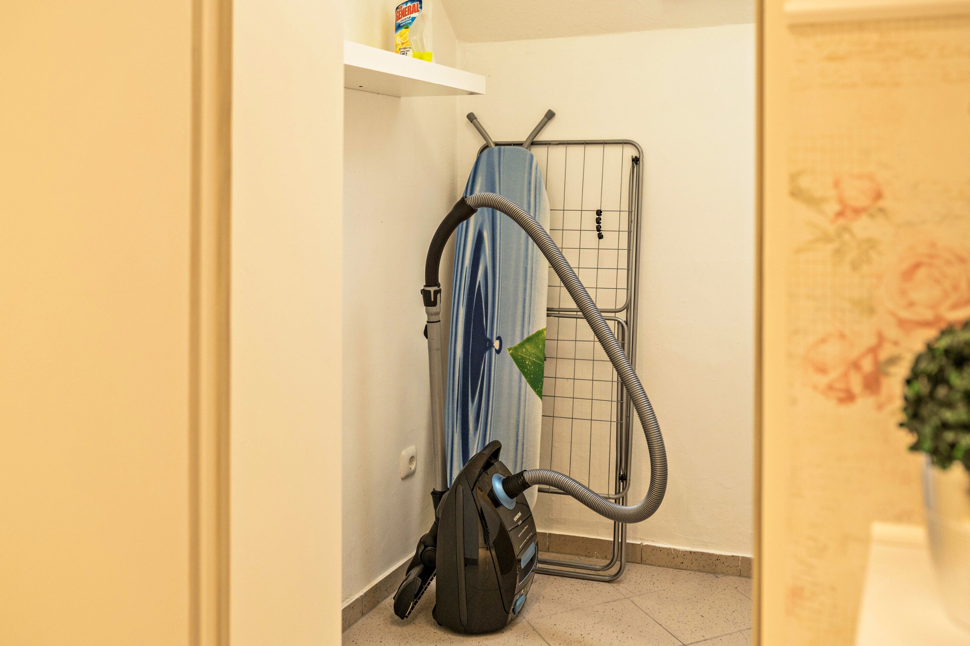 Une pièce contenant un aspirateur, un étendoir et une étagère avec un produit de nettoyage.