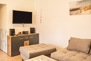 Ein Wohnzimmer mit Flachbildfernseher, Lautsprechern, einer Holzkassette und einem beigefarbenen Sofa.