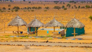 A desert landscape with four thatched-roof huts, each with a small table and chairs. - Amanya  1-Bed Elephant Suite Tent (Amboseli)