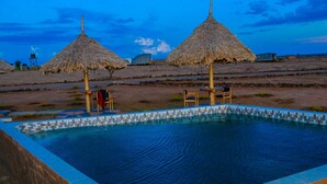 A swimming pool with a tiled edge, surrounded by thatched umbrellas and wooden chairs. - Amanya  1-Bed Elephant Suite Tent (Amboseli)