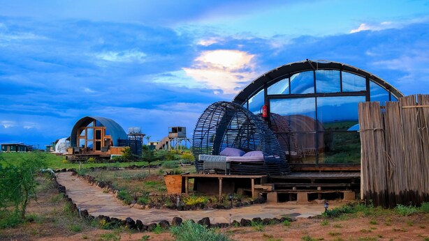 A modern, dome-shaped building with a glass facade, surrounded by a natural landscape and a clear sky. - Amanya  1-Bed Elephant Suite Tent (Amboseli)