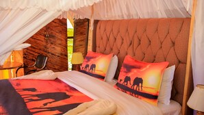 A bed with a colorful blanket, two pillows with desert scenes, a tufted headboard, and a chair. - Amanya  1-Bed Elephant Suite Tent (Amboseli)