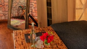 Une pièce chaleureuse avec un mur en pierre, une armoire en bois et une petite table sur laquelle se trouvent une bouteille et des fleurs.