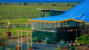 Un bâtiment écologique, doté d’un toit bleu, entouré d’un jardin bien entretenu où poussent différentes espèces de plantes, et offrant une vue dégagée sur le paysage environnant.