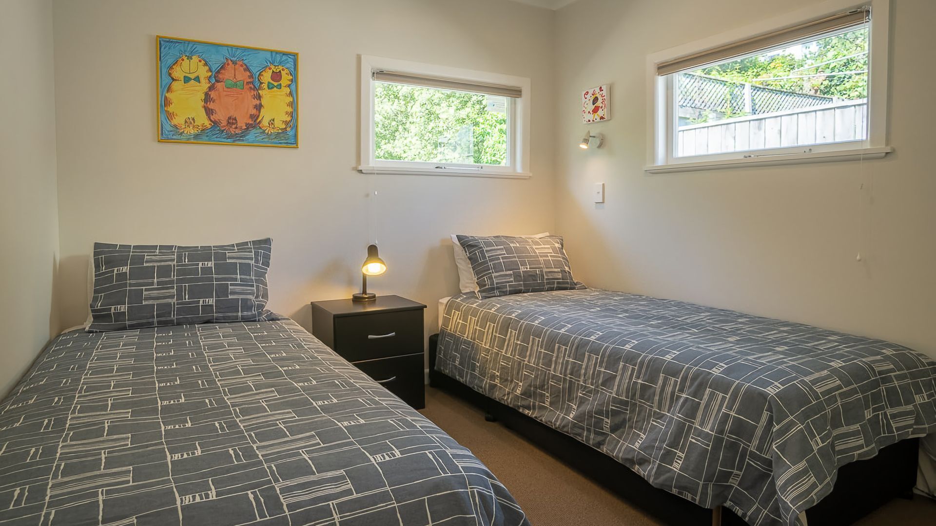 A bedroom with two beds, a nightstand, a lamp, a window, and a painting on the wall.