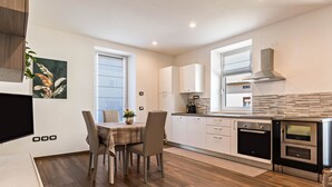 Une cuisine moderne avec des meubles blancs, une table à manger avec des chaises et un four encastré.