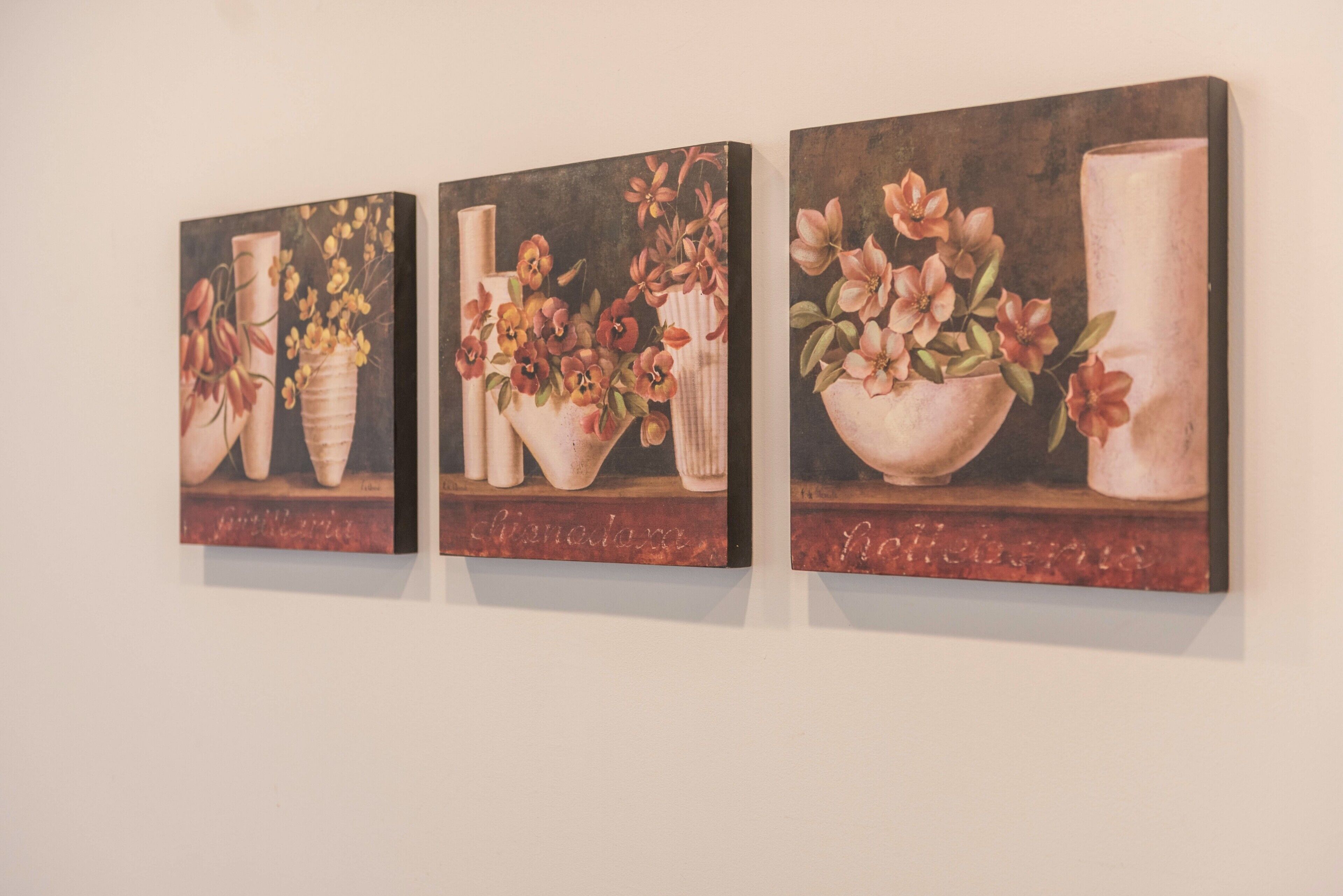 Drei Bilder von floralen Kompositionen an einer Wand.
