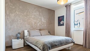 Une chambre à coucher avec un lit, une table de chevet, une lampe et une fenêtre avec des rideaux.